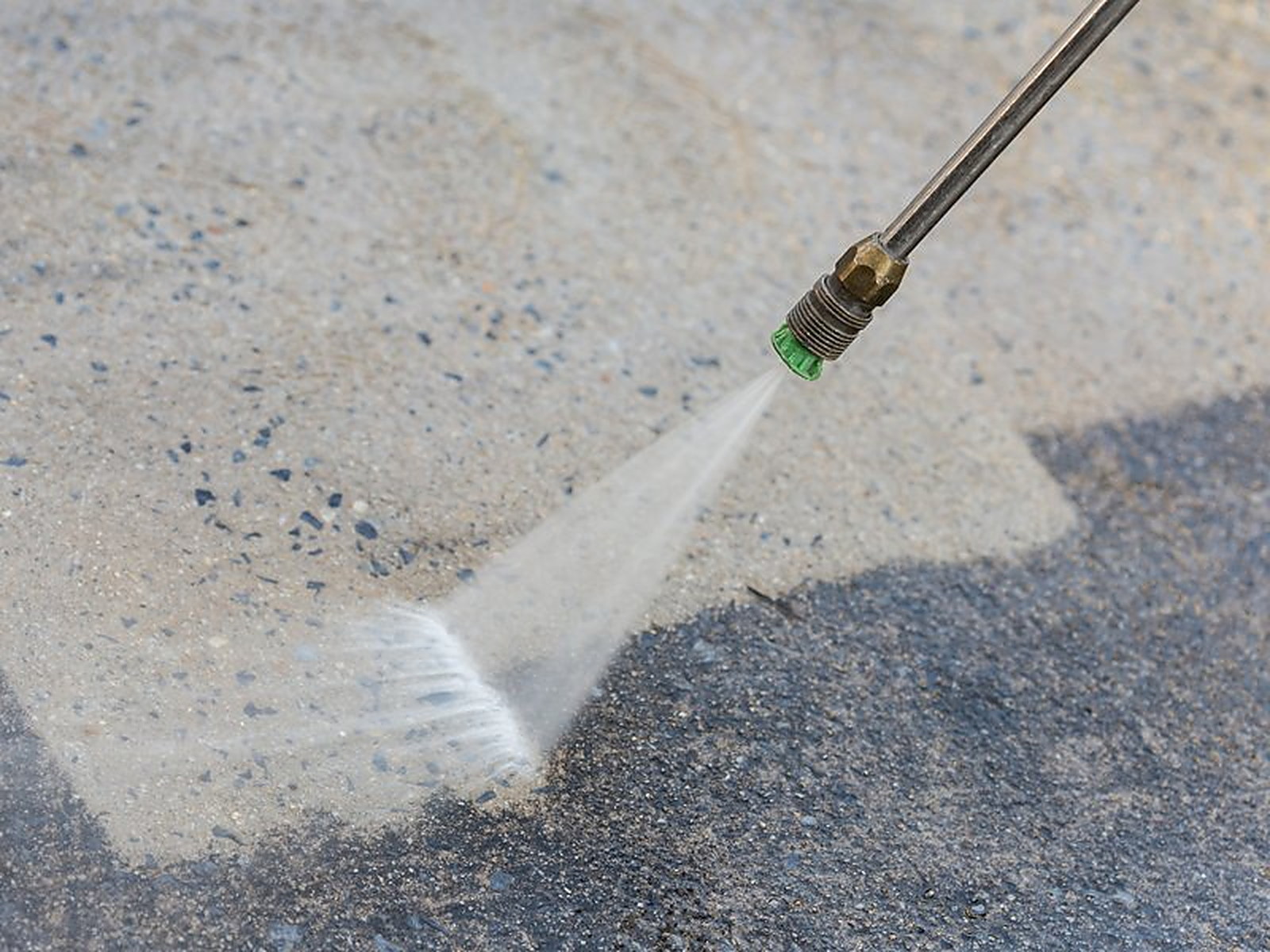 A pressure washer fan jet cutting a pale line across gray concrete