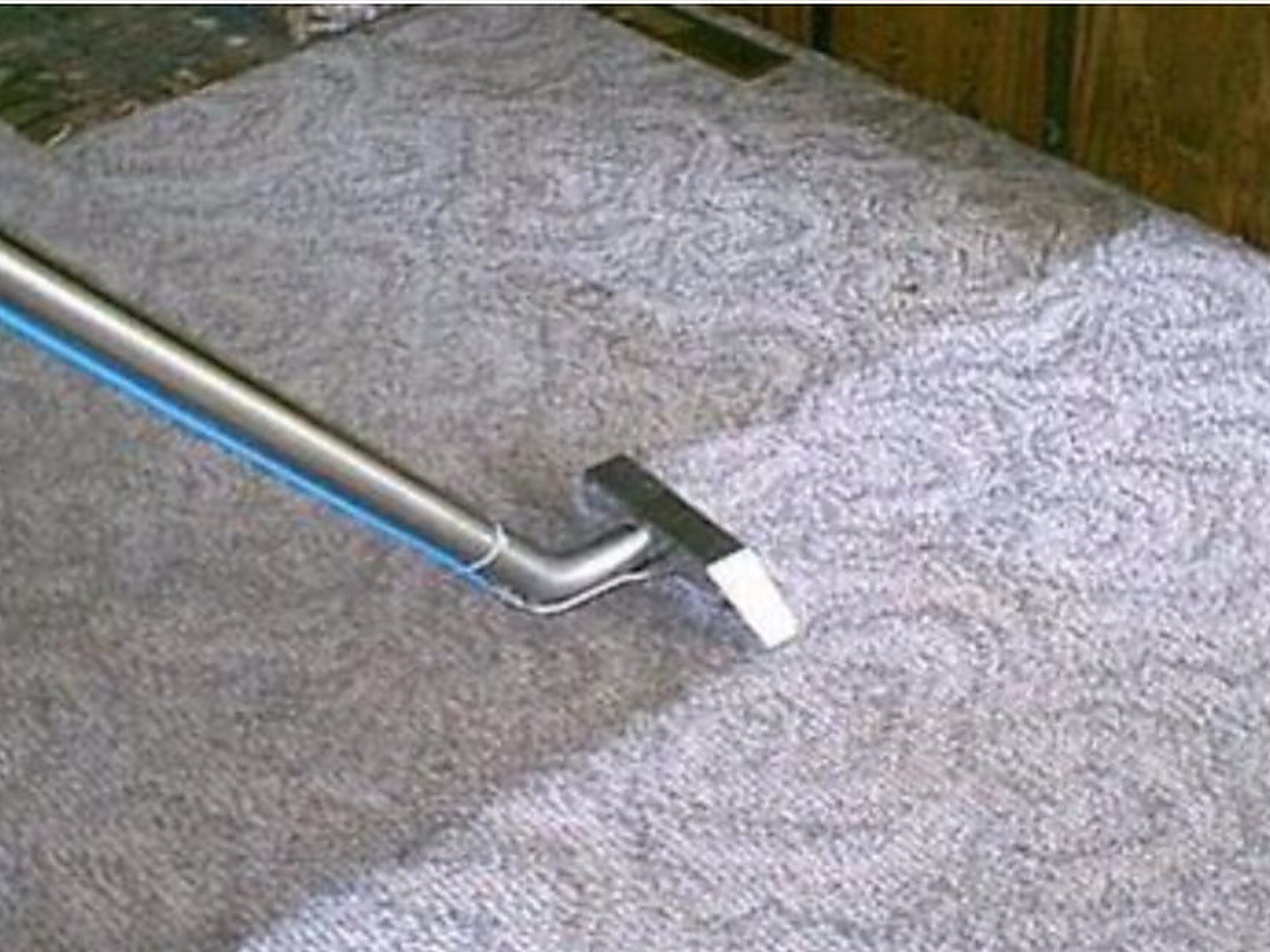 A cleaning wand head on gray patterned carpet with the blue solution line taped along the tube